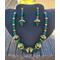 Emerald and gold necklace and earrings in the shade. Deep emerald green beads and bright gold components against the black jewelry display.